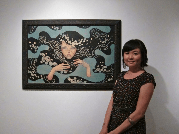 Audrey Kawasaki posant à côté d'une de ses œuvres lors d'une exposition